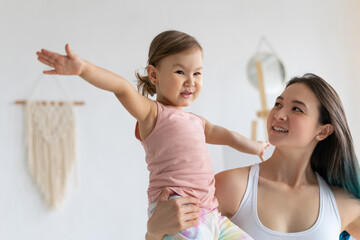 Young mother with little daughter practice yoga home. Warrior pose.