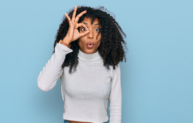 Young african american girl wearing casual clothes doing ok gesture shocked with surprised face, eye looking through fingers. unbelieving expression.