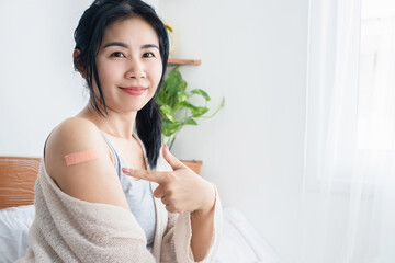 beautiful Asian woman pointing arm after getting vaccinated for anti coronavirus or covid-19,...