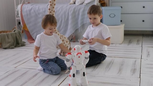 A little boy and a girl are playing at home with a radio-controlled robot sitting on a wooden floor in the bedroom.