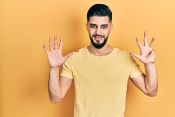 Handsome man with beard wearing casual yellow t shirt showing and pointing up with fingers number nine while smiling confident and happy.