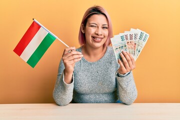 Hispanic woman with pink hair holding czech republic flag and koruna banknotes winking looking at...