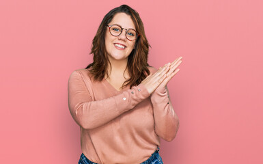 Young plus size woman wearing casual clothes and glasses clapping and applauding happy and joyful, smiling proud hands together