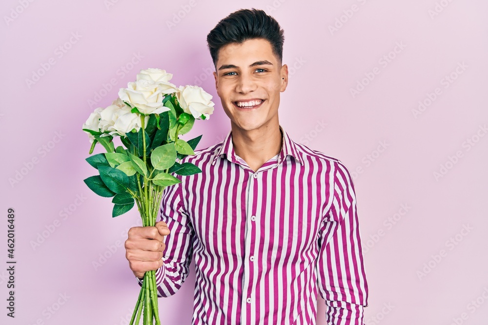 Sticker Young hispanic man holding flowers looking positive and happy standing and smiling with a confident smile showing teeth