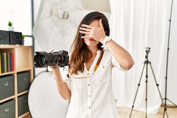 Beautiful caucasian woman working as photographer at photography studio covering eyes with hand, looking serious and sad. sightless, hiding and rejection concept - obrazy, fototapety, plakaty