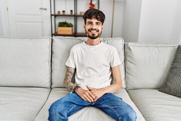 Young hispanic man smiling happy sitting on the sofa at home.