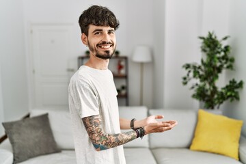 Fototapeta premium Hispanic man with beard at the living room at home pointing aside with hands open palms showing copy space, presenting advertisement smiling excited happy