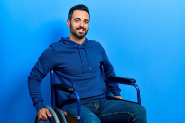 Handsome hispanic man with beard sitting on wheelchair with a happy and cool smile on face. lucky...