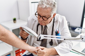 Middle age grey-haired man wearing dermatologist uniform examining skin arm using loupe at...