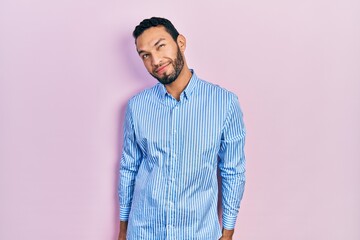 Hispanic man with beard wearing casual blue shirt smiling looking to the side and staring away thinking.
