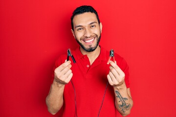 Hispanic man with beard holding battery clamps smiling with a happy and cool smile on face. showing teeth.