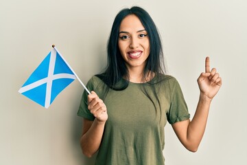 Young hispanic girl holding scotland flag smiling happy pointing with hand and finger to the side