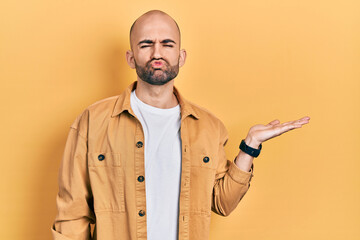 Young bald man presenting with open palms, holding something looking at the camera blowing a kiss being lovely and sexy. love expression.