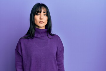 Young brunette woman with bangs wearing turtleneck sweater relaxed with serious expression on face....