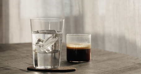 making espresso tonic, add ice cube in tumbler glass on black wood table