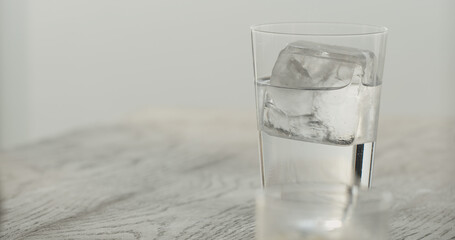 clear ice cube in tumbler glass with tonic on black oak table