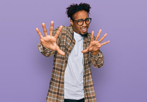 Young african american man with beard wearing casual clothes and glasses afraid and terrified with fear expression stop gesture with hands, shouting in shock. panic concept.