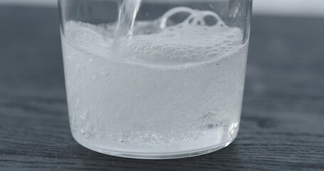 pour tonic in tumbler glass on black wood table closeup