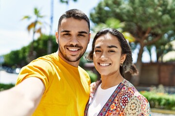 Young latin couple smiling happy and hugging making selfie by the camera at the city.