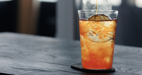 pour tonic water over clear ice ball in tumbler glass on black oak table