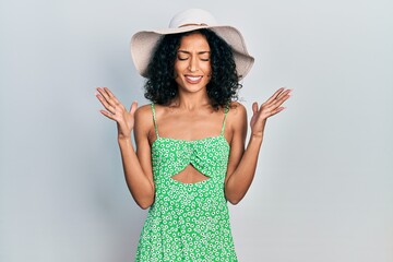 Young latin girl wearing summer hat celebrating mad and crazy for success with arms raised and...