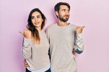 Young hispanic couple wearing casual clothes smiling with happy face looking and pointing to the side with thumb up.