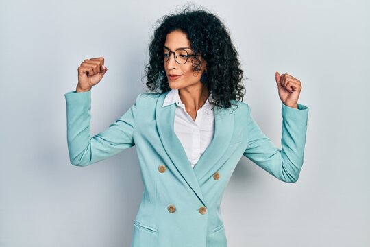 Young latin girl wearing business clothes and glasses showing arms muscles smiling proud. fitness concept.