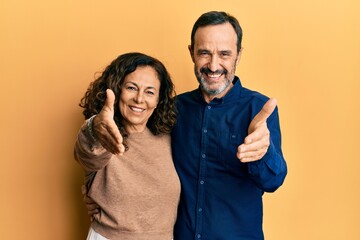 Middle age hispanic couple wearing casual clothes smiling friendly offering handshake as greeting and welcoming. successful business.