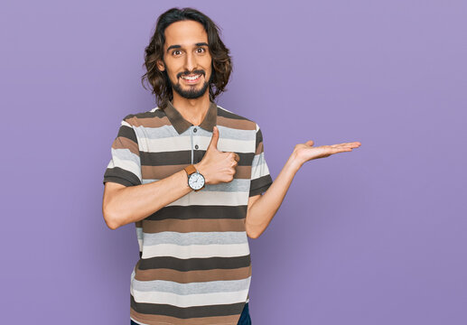 Young hispanic man wearing casual clothes showing palm hand and doing ok gesture with thumbs up, smiling happy and cheerful