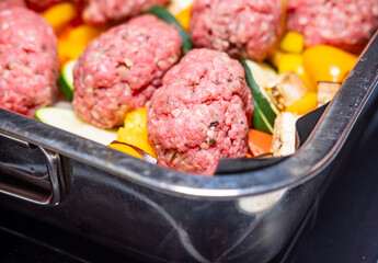 Close and selective focus on raw kofte meatballs on a tray of healthy Mediterranean vegetables comprising yellow pepper, red pepper, courgettes, red onion and aubergine ready for roasting the oven