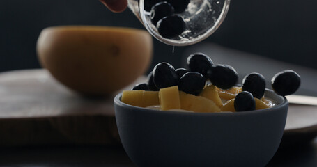 put fresh blueberries over thai mango in natural organic yogurt in blue bowl