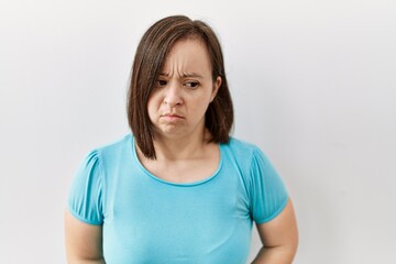 Young down syndrome woman standing over isolated background with hand on stomach because indigestion, painful illness feeling unwell. ache concept.