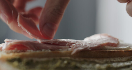man put prosciutto cotto on baguette with cream cheese to make sandwich closeup