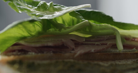 Obraz premium put baby romaine leaves on prosciutto cotto on baguette with cream cheese to make sandwich closeup