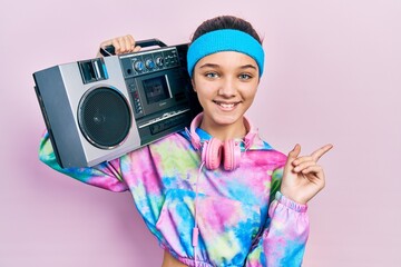 Young brunette girl wearing workout clothes and holding boombox smiling happy pointing with hand...