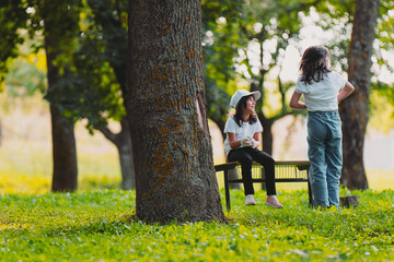 Fototapeta premium Close up photo of two girls outdoors, one girl posing standing with the back to the camera and another girl is sitting on a bench, resting after voluntary work for gathering garbage.