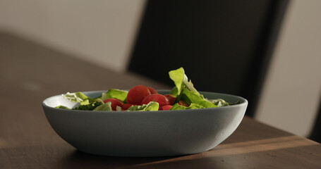 put cherry tomatoes in blue bowl on walnut table making salad