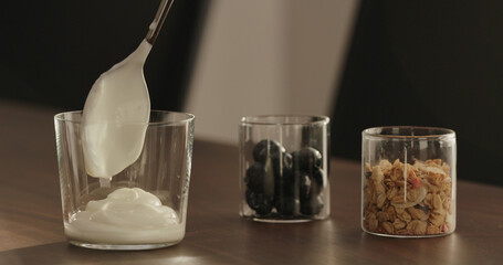 make granola with yogurt in tumbler glass on walnut table
