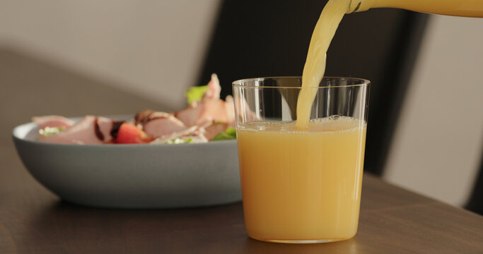 pour orange juice in tumbler glass on black walnut table with salad on background