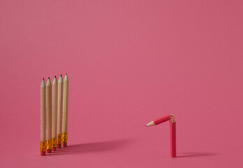 Broken pink wooden crayon in front of pencils on pink background. Minimal concept.