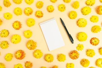 White notebook for notes with pen in round frame made of yellow chrysanthemum flowers on light yellow background. Floral natural pattern.