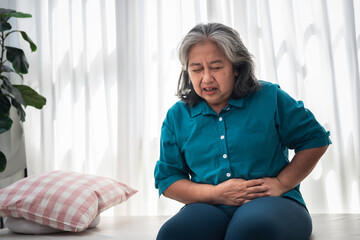 Asian ederly woman sitting on the bed is having a stomachache Due to Gastritis disease, on white...