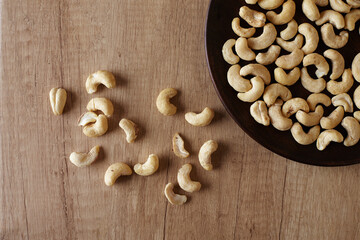 Tasty cashew nuts on a wooden plate on a wooden table, top view. Space for text