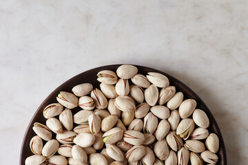 Tasty pistachio nuts on a wooden plate on a wooden table, top view. Space for text