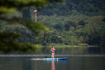Fototapeta na wymiar A woman stand up paddle boards (SUP) on a calm Lake