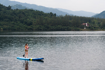 A woman stand up paddle boards (SUP) on a calm Lake
