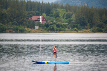 A woman stand up paddle boards (SUP) on a calm Lake