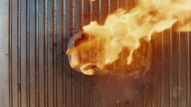 Grilled beef tenderloin. Process of flaming. Man pours alcohol on the meat lying on the grill and roasts steak. Flambe, flamber. Closeup