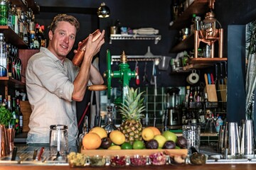 View of a cheerful man working as bartender in a colourful cocktail bar, view of a professional...