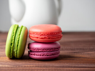 Colorful delicious macaroons lie on a wooden table. In the background is a white teapot